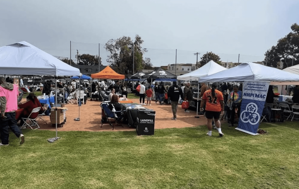 Outdoor market with tents and people browsing stalls on a cloudy day.